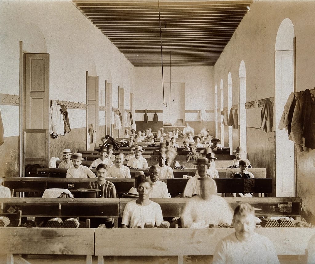 Fotografia histórica em preto e branco de um salão comprido com pessoas em bancadas