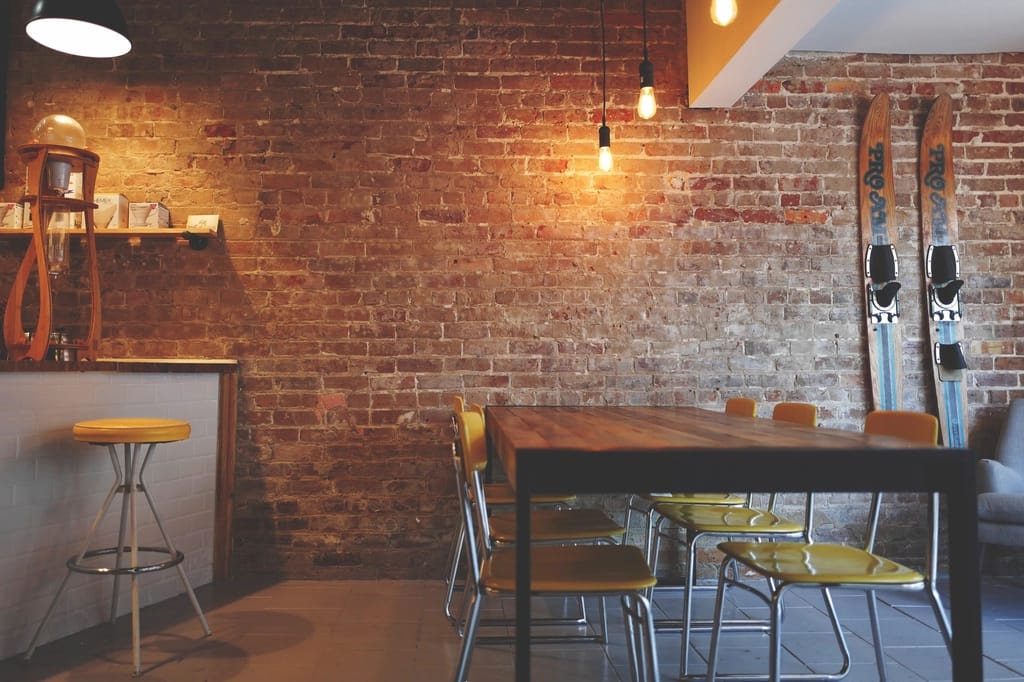 Interior de um café com parede de tijolos aparentes, mesa comprida e banquetas